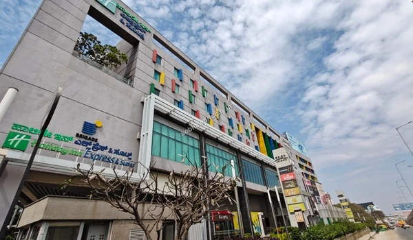 The iconic Brigade clock tower standing prominently next to the multi-level shopping complex, serving as a distinct landmark for residents of Sobha World City