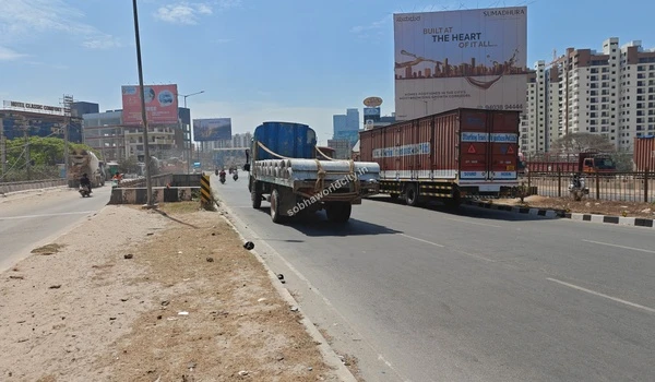 Commercial trucks and heavy vehicles moving smoothly on the wide highway leading to Hoskote, ensuring robust logistical connectivity for Sobha World City.