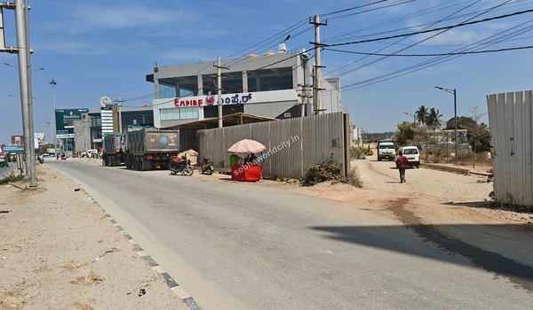 Heavy vehicles and local traffic passing by the barricaded entrance of the Sobha World City site on Old Madras Road.
