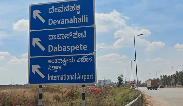Curved highway stretch featuring a prominent Devanahalli direction board, emphasizing the strong road network around Sobha World City.