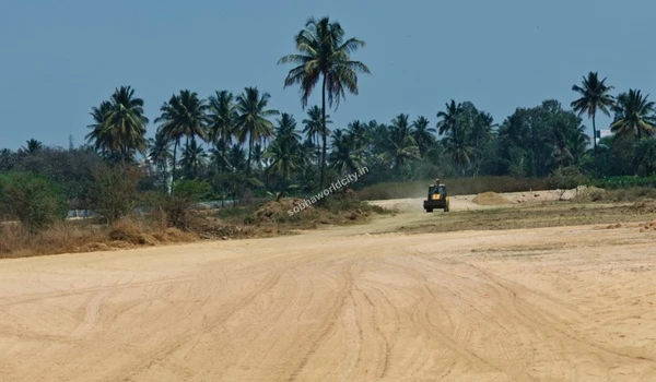 Yellow backhoe loader flattening the sandy dirt track at the Sobha World City construction site