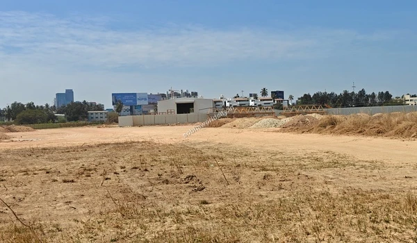 Flat sandy area with dry grass in the foreground looking towards a temporary metal shed and barricades at Sobha World City