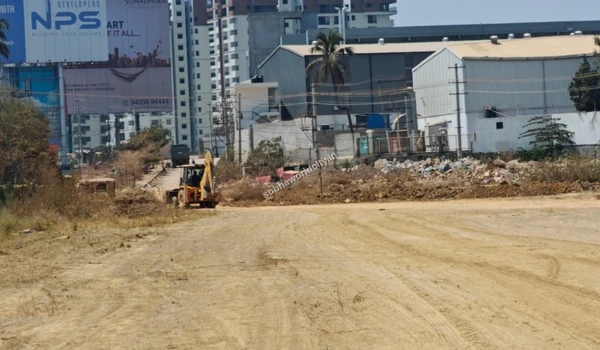 Backhoe loader actively moving earth and leveling the ground near the boundary of Sobha World City
