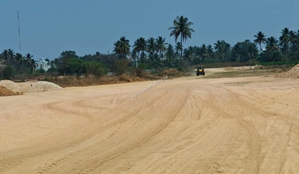 Wide view of the extensive sandy trail and distant construction machinery at Sobha World City