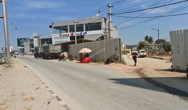View of the Sobha World City entrance path located adjacent to the bustling Old Madras Road highway with local vendor stalls.