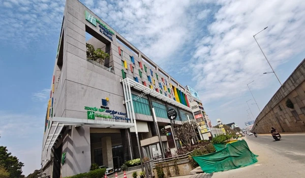 A grand exterior view of Orion Uptown Mall featuring large billboards for Barbeque Nation and Max Fashion, providing a premium shopping experience near Sobha World City