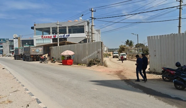Pedestrians and ongoing transit near the Sobha World City project entrance, showcasing the vibrant infrastructure of the Hoskote road network.