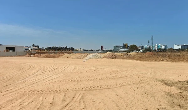 Wide angle view of the extensive sandy expanse with vehicle tracks and distant city buildings at the Sobha World City site
