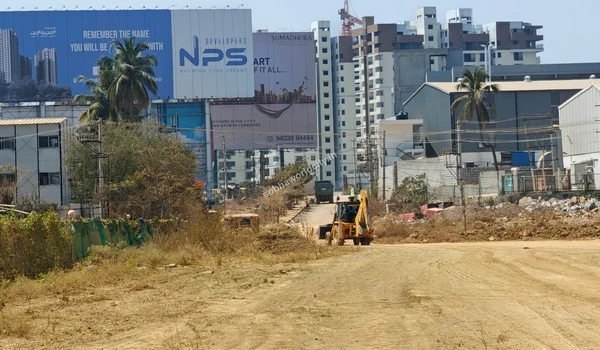 A yellow backhoe loader clearing the dirt pathway with distant billboards and buildings at Sobha World City