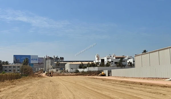 Yellow construction machinery operating on the dirt road leading into the Sobha World City project site
