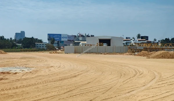 Large curved tire tracks on the sandy ground leading towards a temporary metal storage shed and billboards at Sobha World City