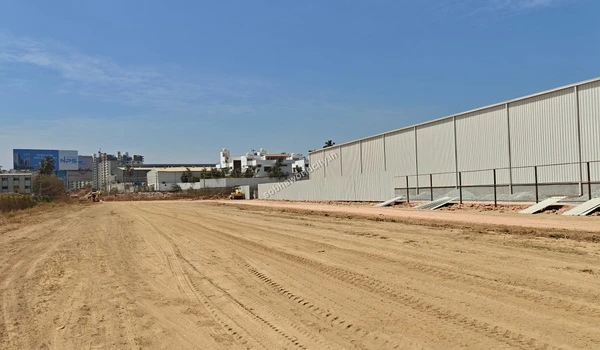 Exterior view of a long white metal construction warehouse situated along the sandy road at Sobha World City